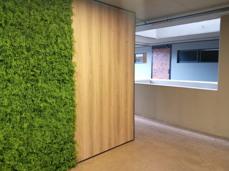 A modern apartment hallway featuring a decorative artificial green wall, wood-look paneling, and polished concrete flooring, leading to an open-air corridor.