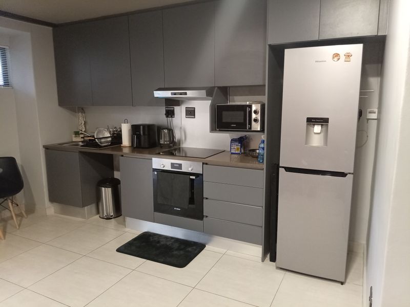 Modern kitchen featuring sleek grey cabinetry, integrated oven, electric hob, extractor fan, built-in microwave, and tiled flooring.