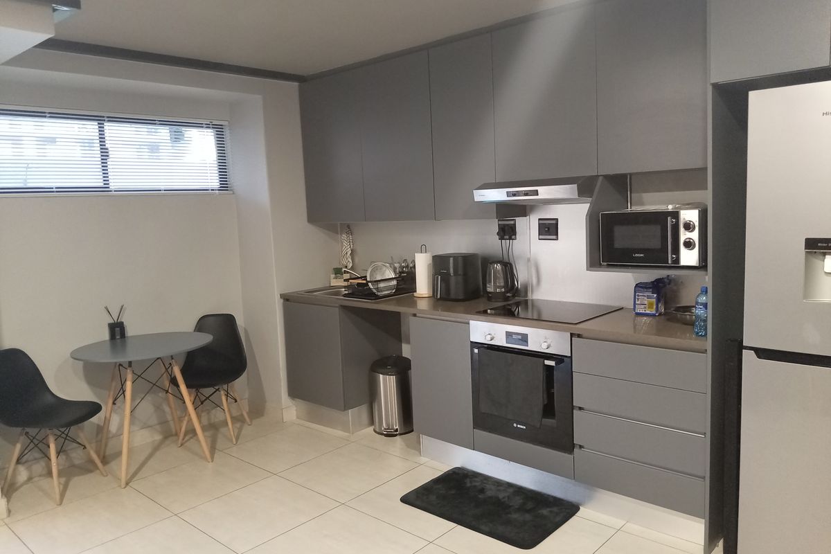 Modern kitchen featuring sleek grey cabinetry, integrated appliances including an oven and cooktop, and neutral tiled flooring.