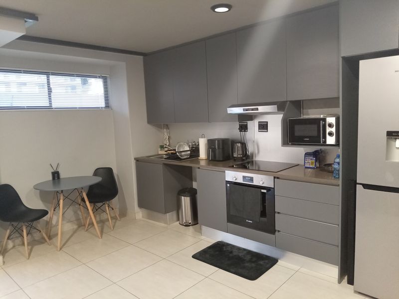 Modern kitchen featuring sleek grey cabinetry, integrated appliances including an oven and cooktop, and neutral tiled flooring.