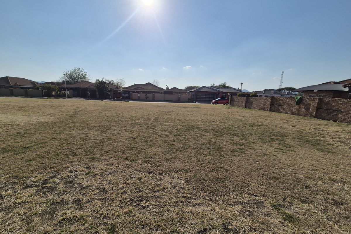 A wide-angle view of a vacant residential plot featuring dry grass and a surrounding brick boundary wall in a suburban neighborhood.