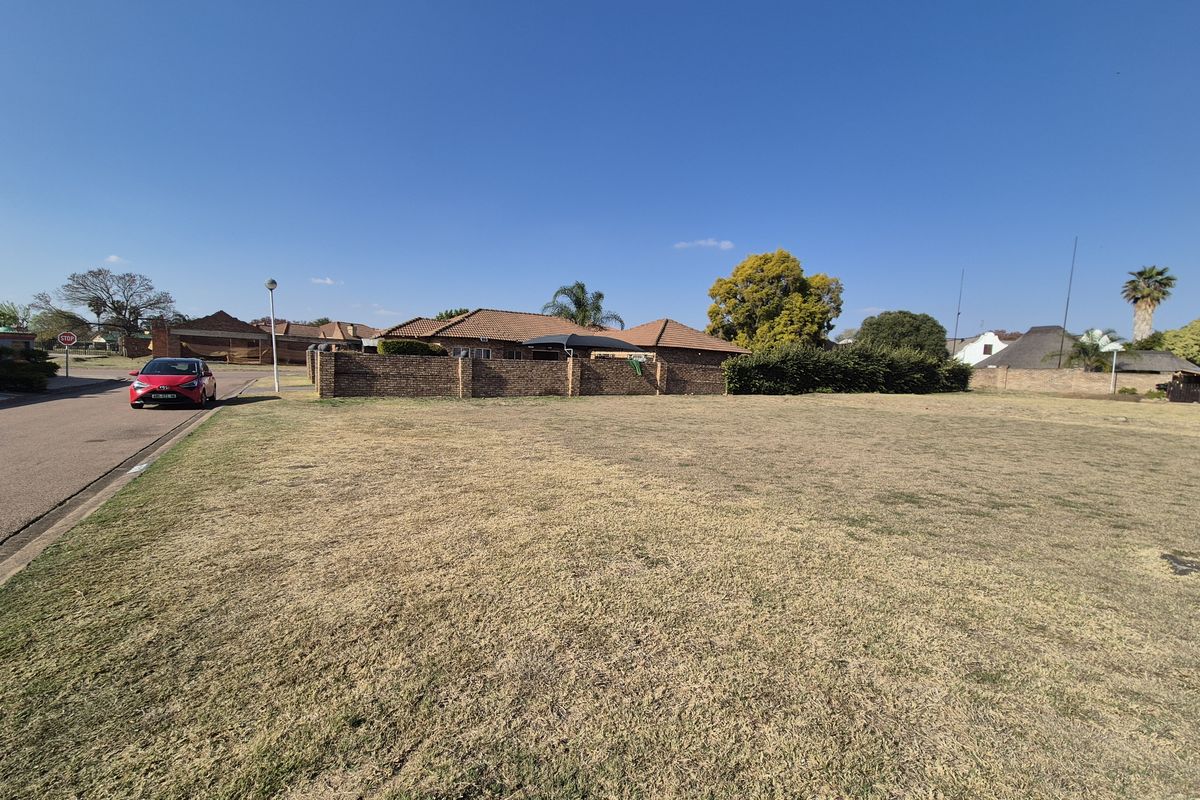 A vacant residential plot of land featuring a level grass surface and a brick boundary wall, situated in a established residential neighborhood.