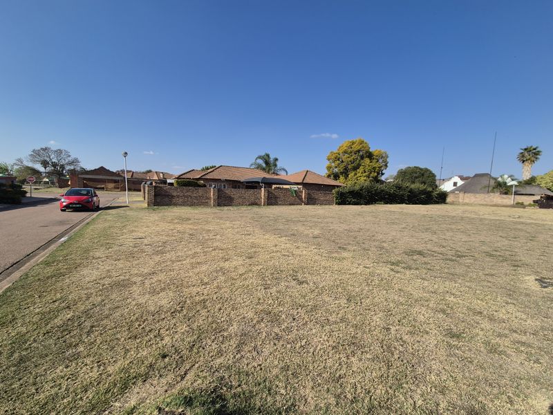 A vacant residential plot of land featuring a level grass surface and a brick boundary wall, situated in a established residential neighborhood.