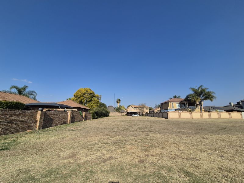 A vacant residential plot featuring a level grass lawn and established boundary walls, situated within an established neighborhood.