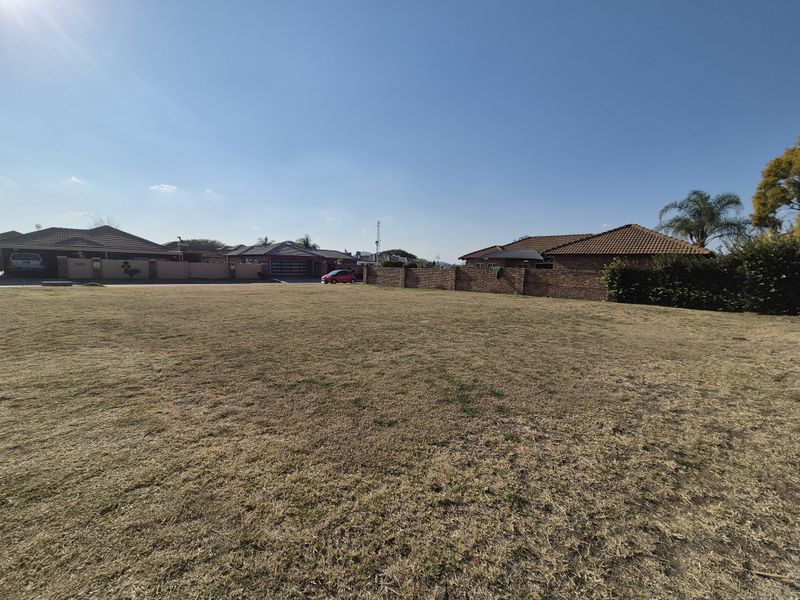A wide-angle view of a vacant residential plot featuring a grass lawn and surrounding boundary walls in a suburban neighborhood.