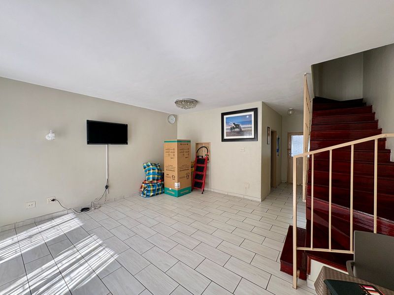 An open-plan living area featuring light-colored floor tiles and a wooden staircase with a metal railing, providing a neutral base for interior design.