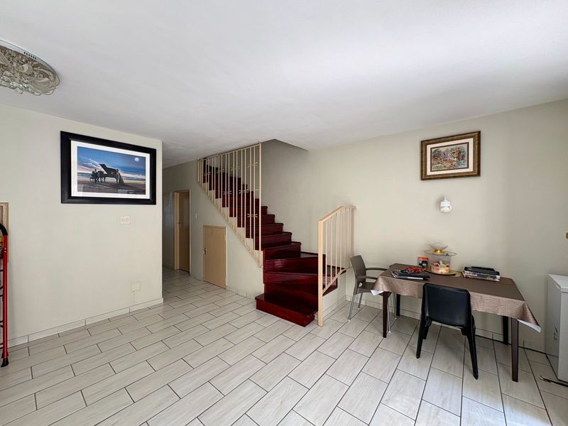 Open plan living area featuring a prominent wooden staircase with metal balustrade and neutral tiled flooring throughout.