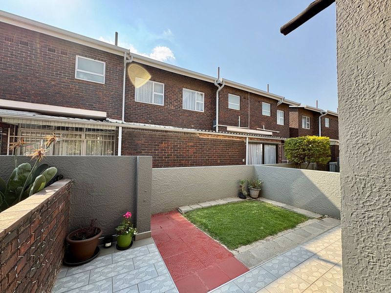 A private rear courtyard featuring a small lawn, paved walkway, and tiled patio area, enclosed by painted boundary walls against a brick townhouse facade.
