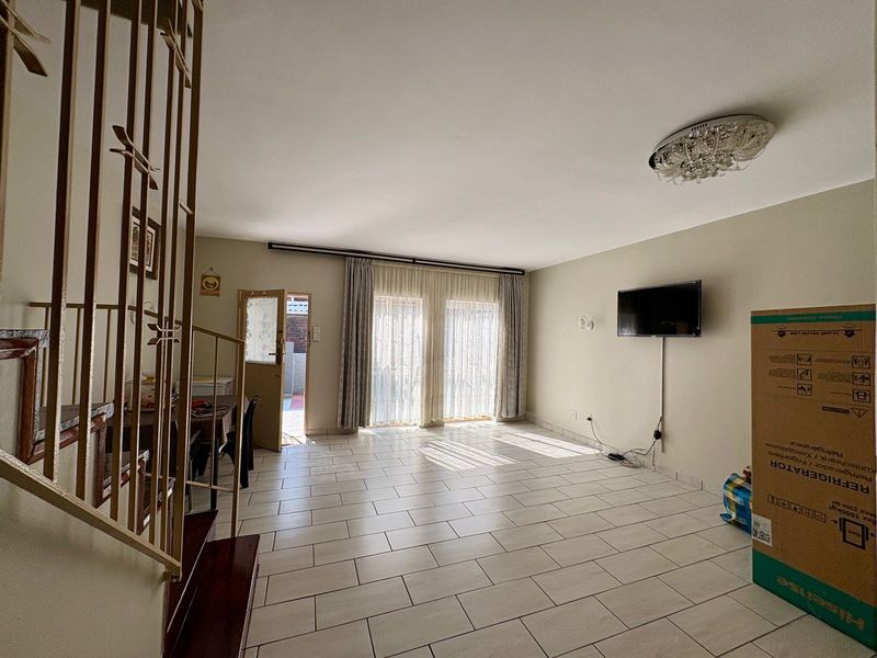 Spacious living area featuring neutral tiled flooring, a staircase with metal balustrades, and sliding glass doors providing access to the exterior.