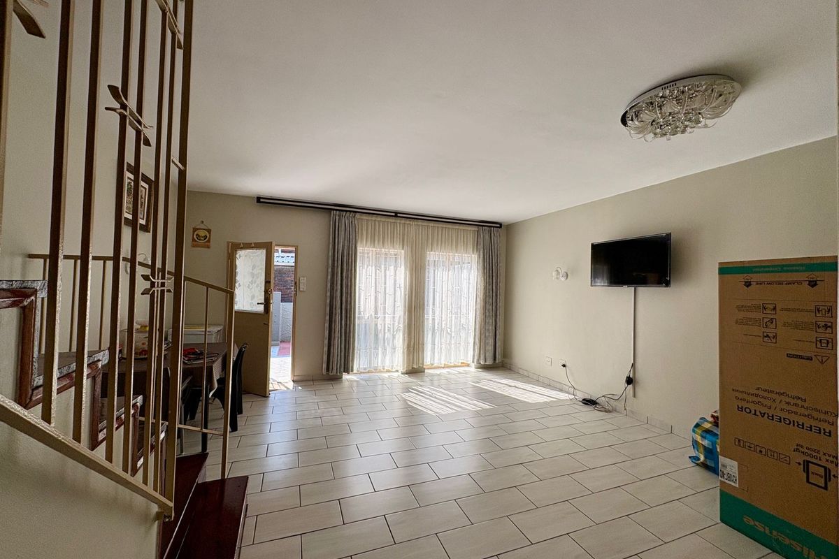 Spacious living area featuring neutral tiled flooring, a staircase with metal balustrades, and sliding glass doors providing access to the exterior.