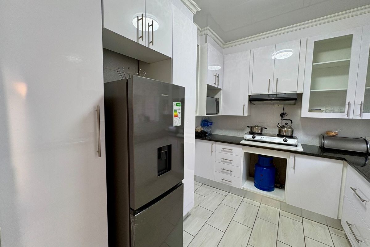 Modern kitchen featuring glossy white cabinetry, black granite countertops, gas hob, and extractor fan, with tiled flooring throughout.