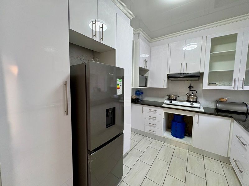 Modern kitchen featuring glossy white cabinetry, black granite countertops, gas hob, and extractor fan, with tiled flooring throughout.