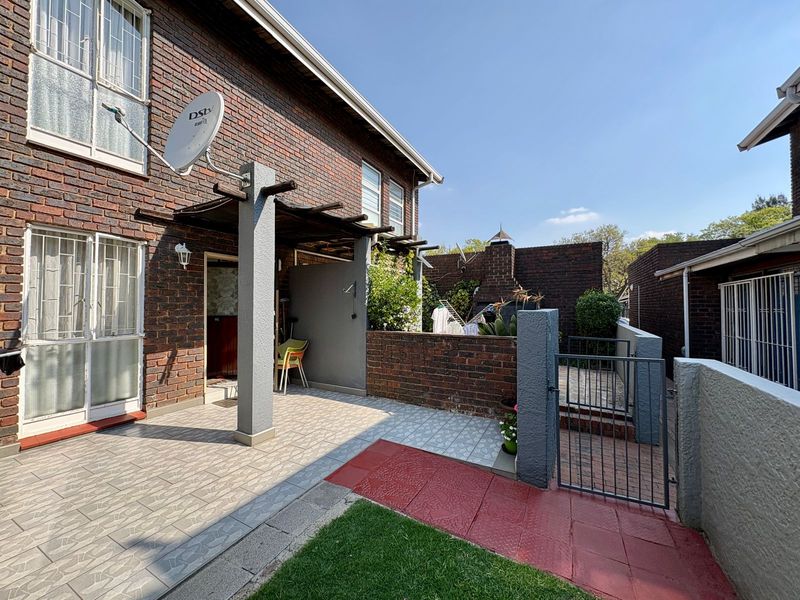 Rear exterior view of a townhouse featuring a brick facade, a paved patio area with a pergola, and a built-in braai facility.