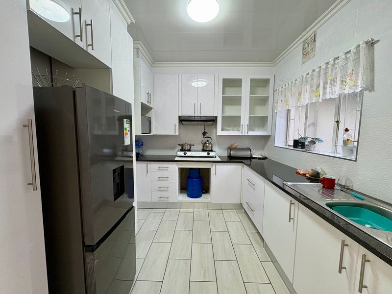 A clean, modern kitchen featuring white cabinetry, dark granite countertops, a gas hob with extractor, and light-toned tiled flooring.