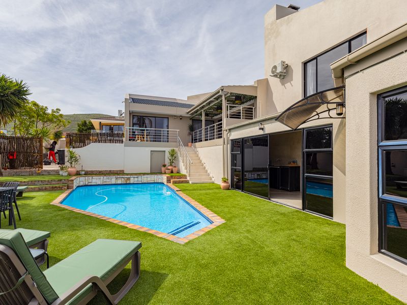 A well-maintained outdoor pool area featuring a swimming pool, artificial lawn, and direct access to the home via sliding glass doors and an external staircase.