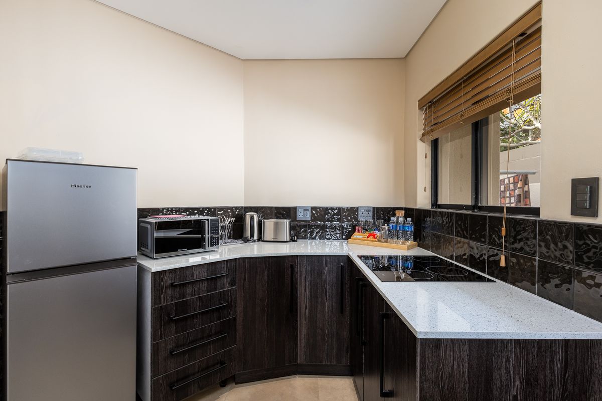 A compact, modern kitchen featuring dark wood cabinetry, light stone countertops, a black tiled backsplash, and a built-in electric hob.
