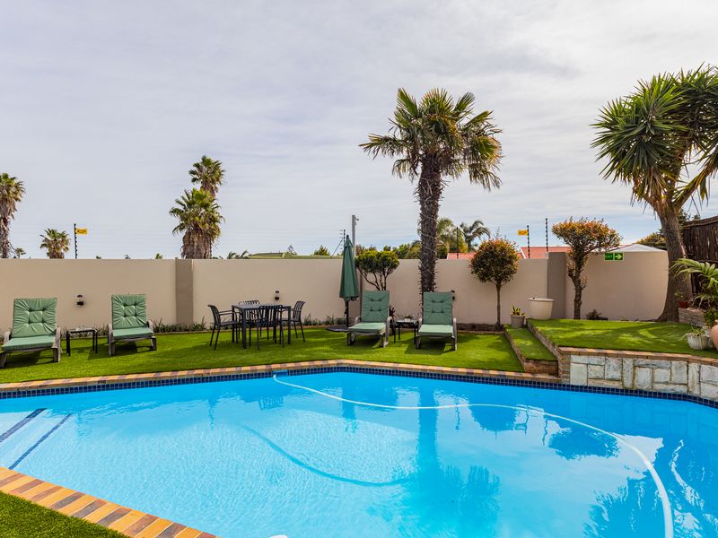 A well-maintained outdoor pool area featuring a swimming pool, artificial lawn, and secure perimeter wall with electric fencing.