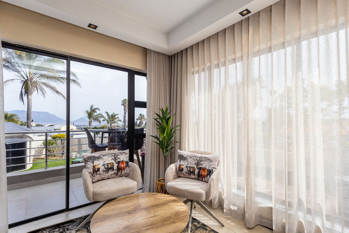 A bright living area featuring large sliding glass doors, floor-to-ceiling curtains, and recessed lighting, offering seamless access to an outdoor balcony.
