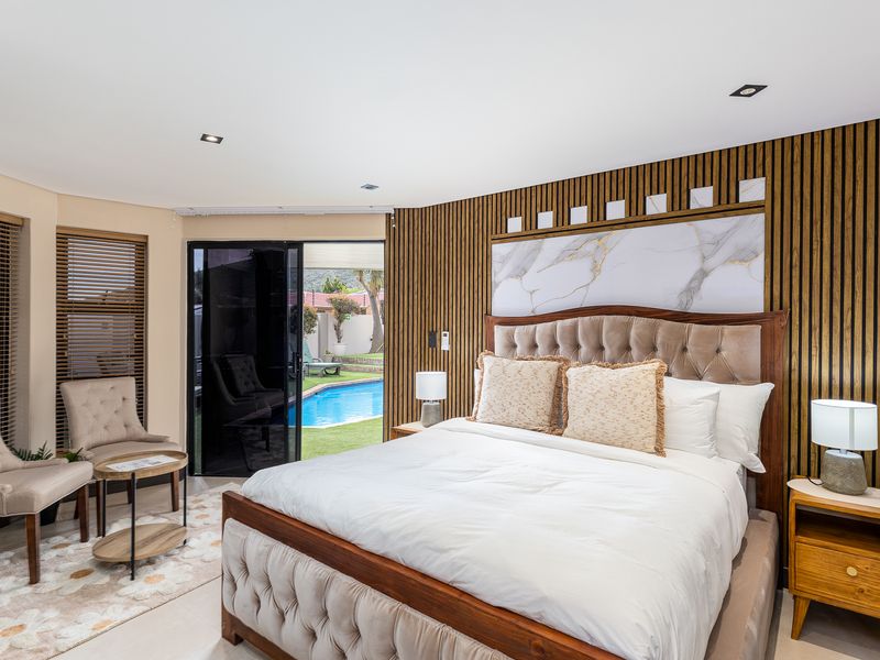 A well-appointed bedroom featuring modern timber slat wall paneling, a marble accent wall, recessed lighting, and direct access to the pool area.