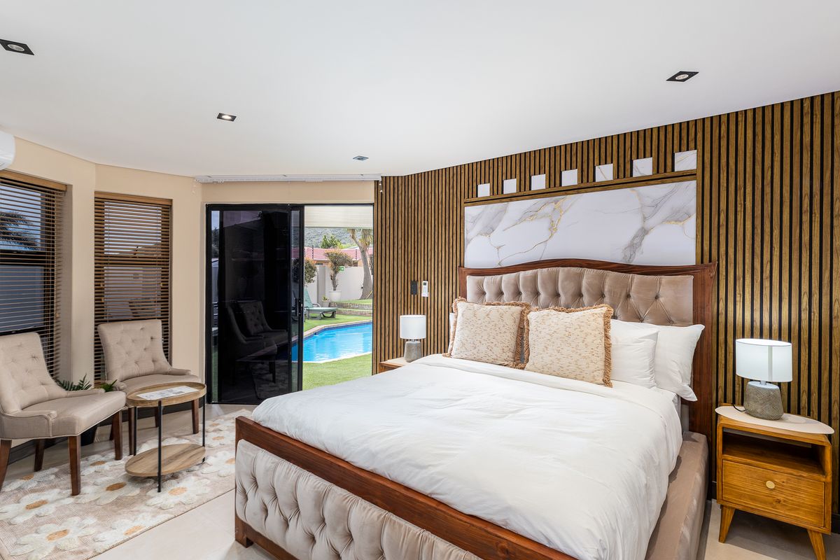 A well-appointed bedroom featuring modern timber slat wall paneling, a marble accent wall, recessed lighting, and direct access to the pool area.