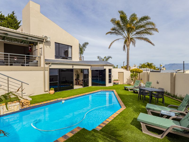 A well-maintained outdoor pool area featuring a swimming pool, artificial lawn, and a covered patio with access to the main house.