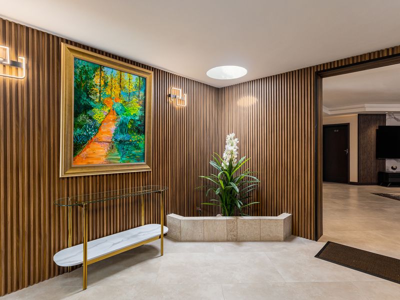 A modern, well-lit entrance hall featuring sophisticated slatted wood wall paneling, a built-in stone planter, and a circular skylight.