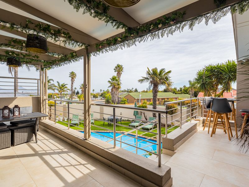 Spacious covered balcony featuring tiled flooring and stainless steel balustrades, overlooking a private swimming pool and landscaped garden area.