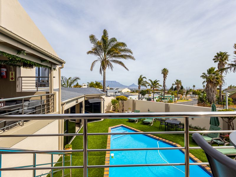 Elevated balcony overlooking a private swimming pool, artificial lawn, and landscaped garden with distant mountain views.