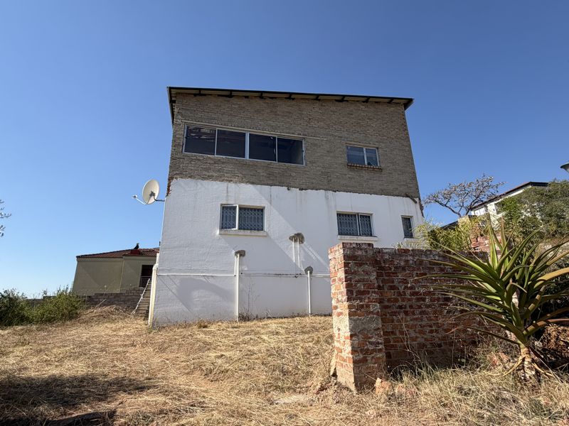 Rear view of a multi-story house featuring exposed brickwork, security bars on windows, and a surrounding brick boundary wall in need of maintenance.