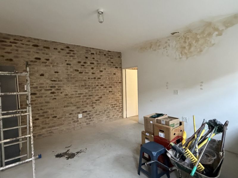 An unfinished living area featuring an exposed brick feature wall, concrete flooring, and visible ceiling water damage requiring repair.