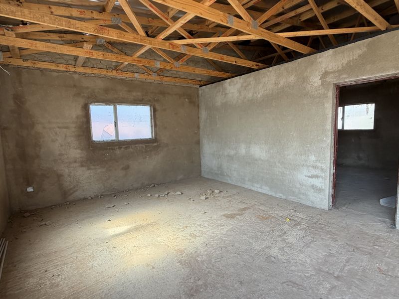 An unfinished interior space featuring exposed timber roof trusses, plastered masonry walls, and cement screed flooring, offering a blank canvas for renovation.