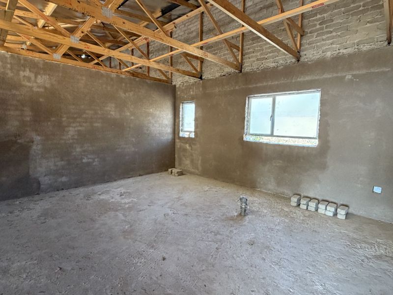 An unfinished interior space featuring exposed timber roof trusses, plastered brick walls, and concrete flooring, offering a blank canvas for renovation.