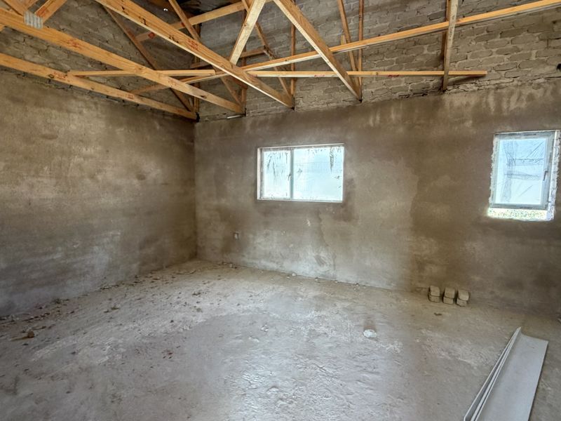 An unfinished room interior featuring exposed timber roof trusses, raw brick walls, and cement flooring, offering a blank canvas for renovation.