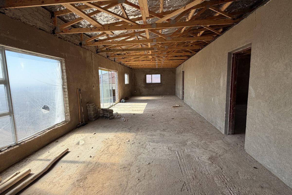 An unfinished open-plan interior space featuring exposed timber roof trusses, plastered walls, and large aluminium windows, currently in a shell construction state.