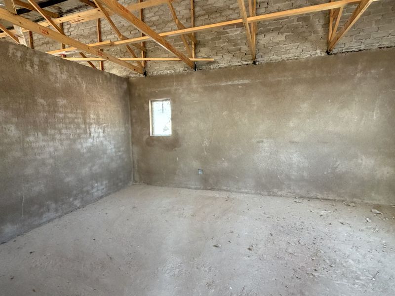 An unfinished interior space featuring exposed timber roof trusses, raw brickwork, and cement screed flooring, offering a blank canvas for renovation.