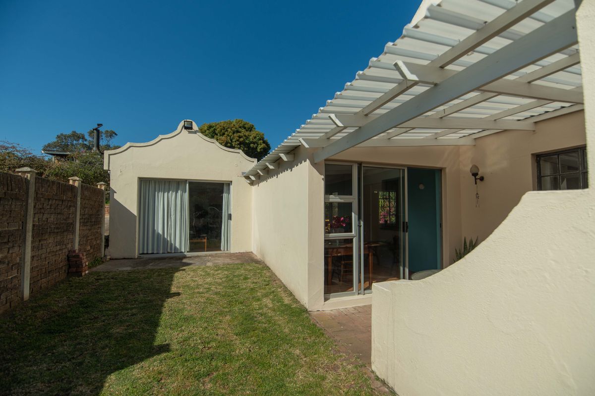 Rear exterior view featuring a paved patio area, a pergola, and a small garden space with a brick boundary wall.