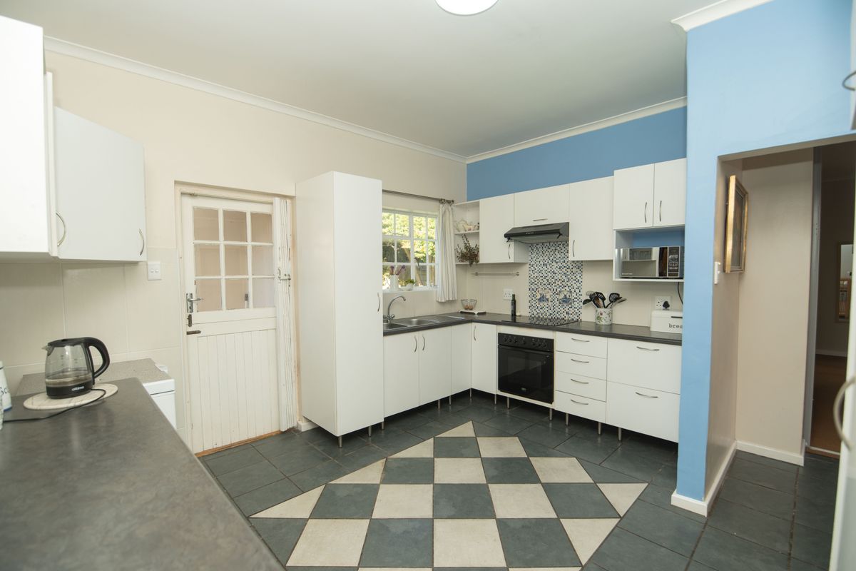 A functional kitchen featuring white cabinetry, dark laminate countertops, a built-in oven with extractor, and a distinctive checkered tile floor with a stable door.