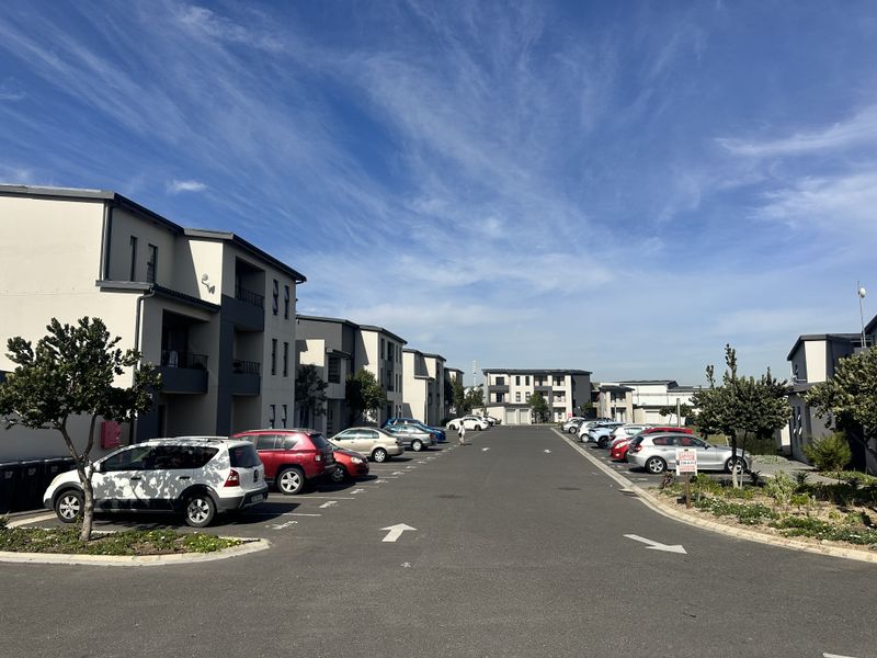 A view of the apartment complex street and parking area, featuring modern multi-story residential buildings and paved parking bays.