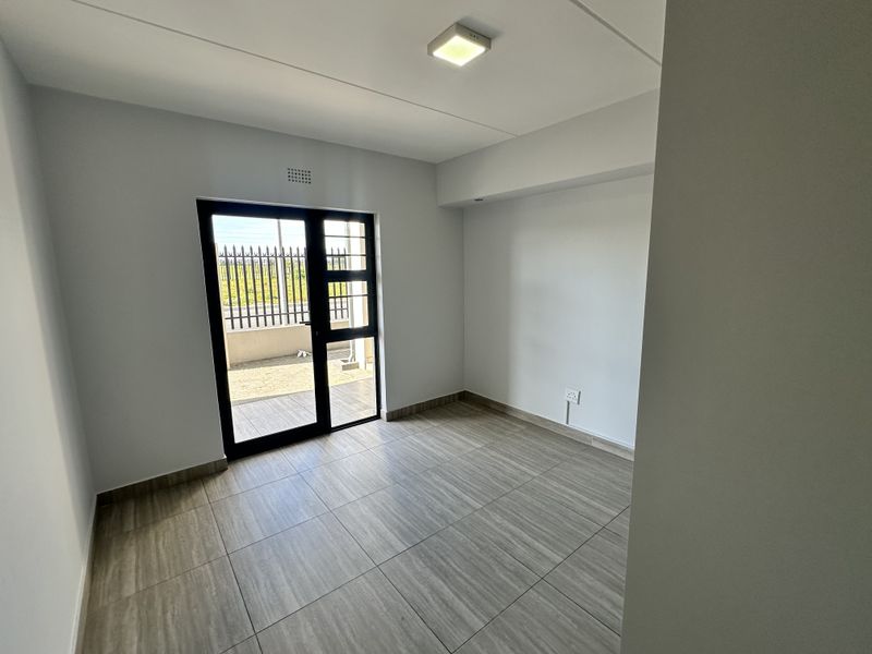 A bright, empty bedroom featuring modern wood-look tiled flooring and a glass door providing access to the exterior.