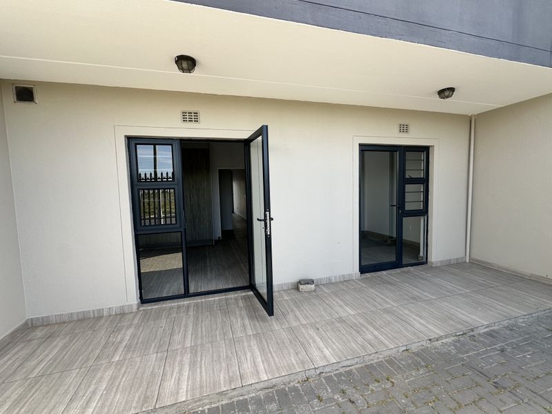 A clean, covered patio area featuring modern tiled flooring and dark aluminium framed glass doors providing access to the interior.