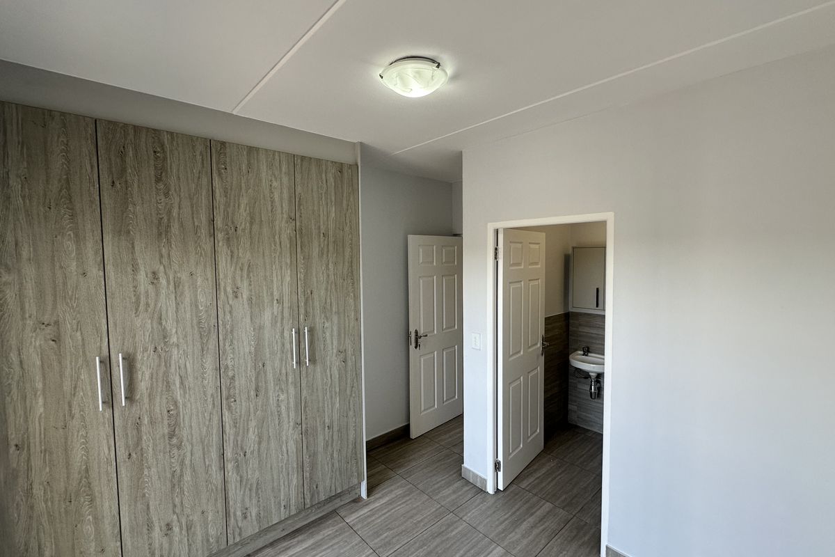 A clean, empty bedroom featuring modern wood-look tiled flooring, built-in cupboards, and direct access to an en-suite bathroom.