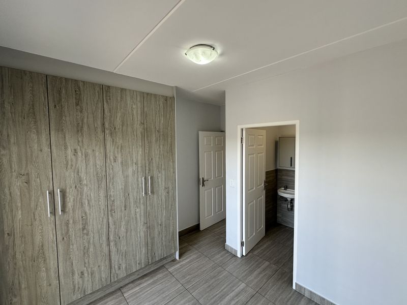 A clean, empty bedroom featuring modern wood-look tiled flooring, built-in cupboards, and direct access to an en-suite bathroom.