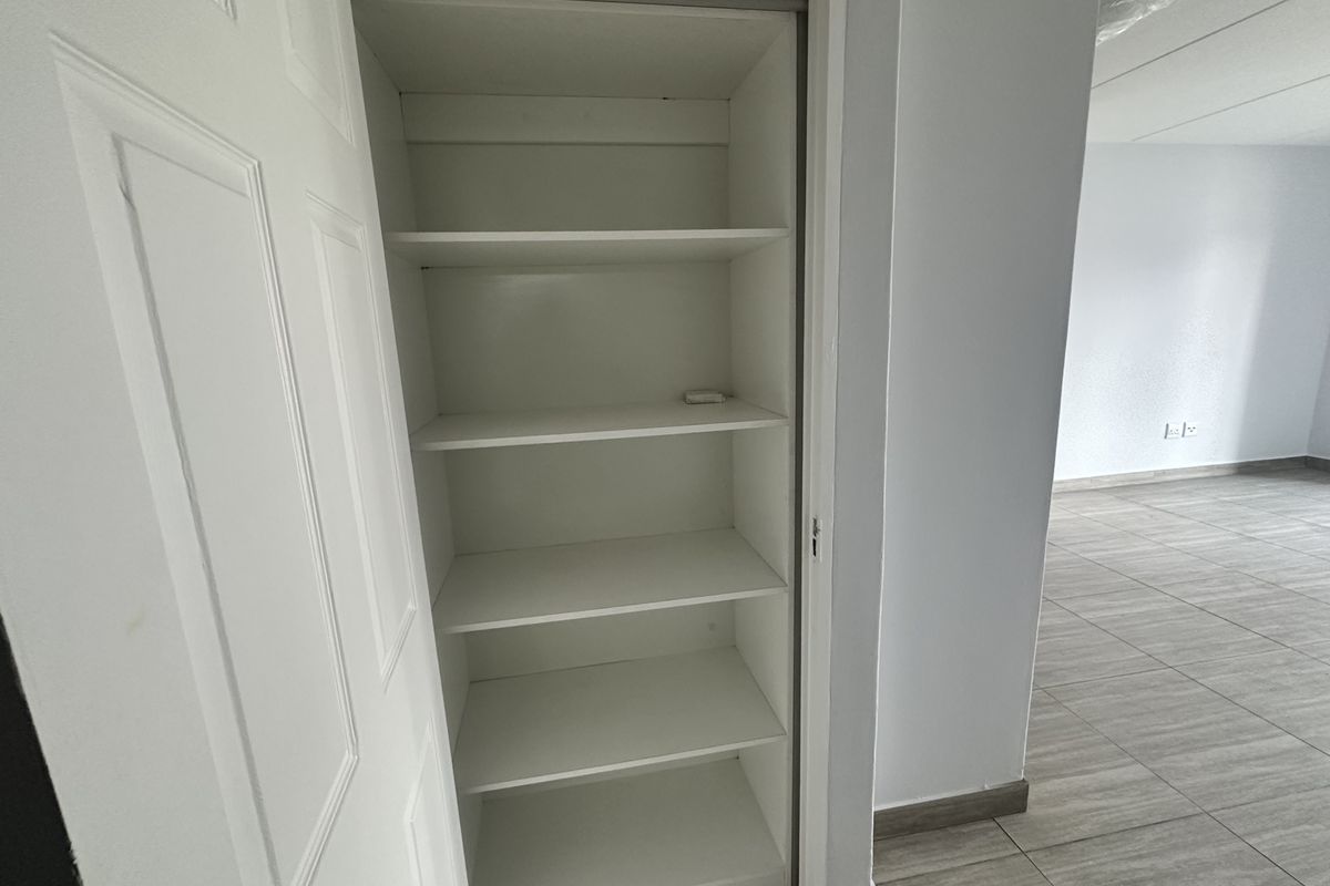 A clean, empty built-in storage closet with multiple fixed shelves, featuring neutral tiled flooring and white interior finishes.