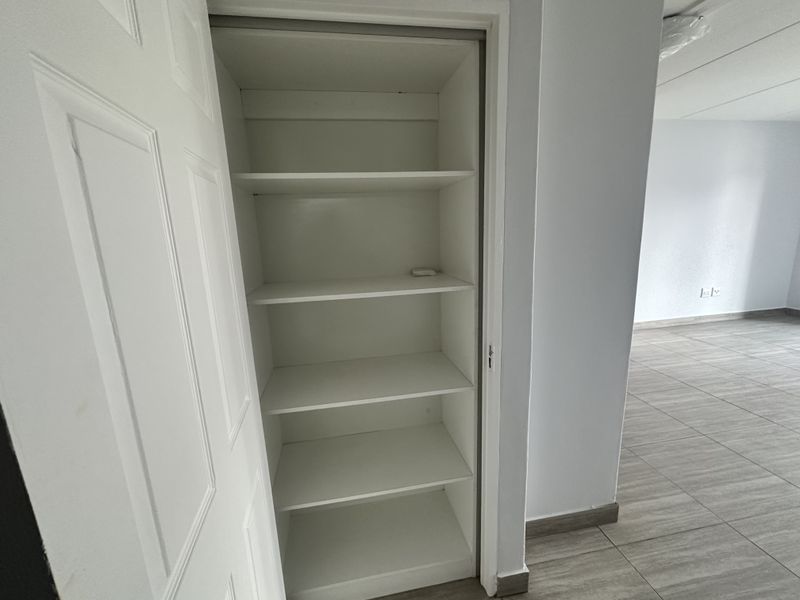 A clean, empty built-in storage closet with multiple fixed shelves, featuring neutral tiled flooring and white interior finishes.