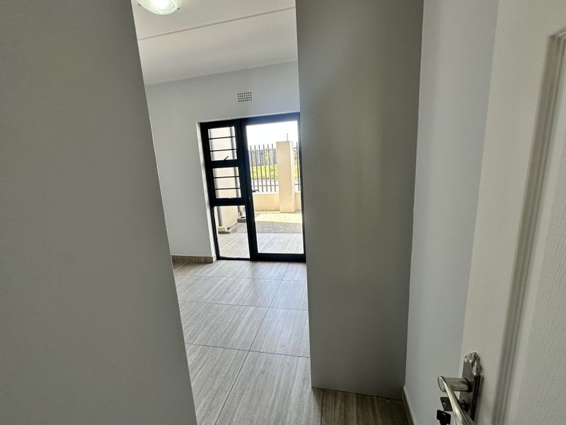 A bright, empty hallway featuring neutral tiled flooring and a sliding glass door providing access to an outdoor area.