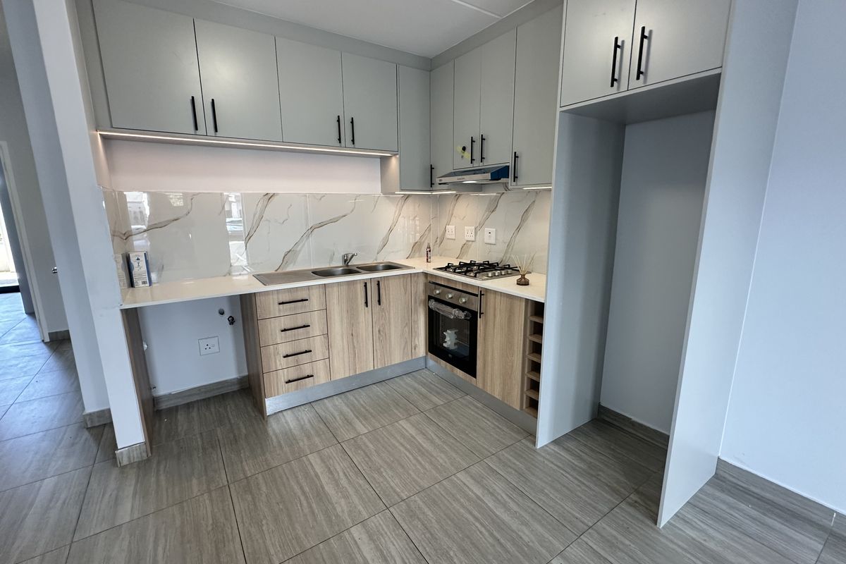 Modern kitchen featuring light wood-tone lower cabinets, grey upper cabinetry, marble-look splashback, gas hob, built-in oven, and integrated extractor fan.