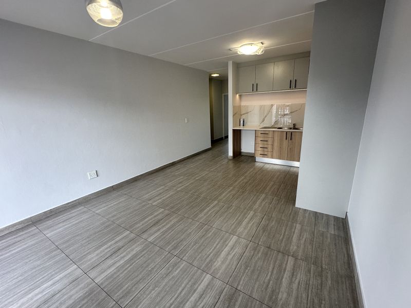 An open-plan living area featuring modern tiled flooring, neutral walls, and a compact kitchenette with built-in cabinetry and a marble-look splashback.