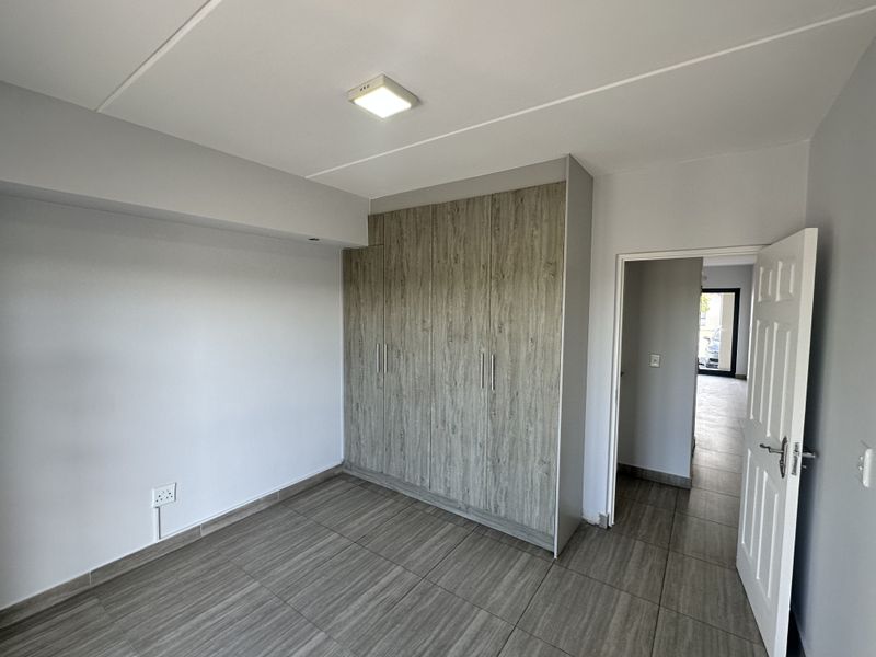 A clean, modern bedroom featuring wood-look tiled flooring and ample built-in cupboard storage, offering a neutral and well-maintained living space.