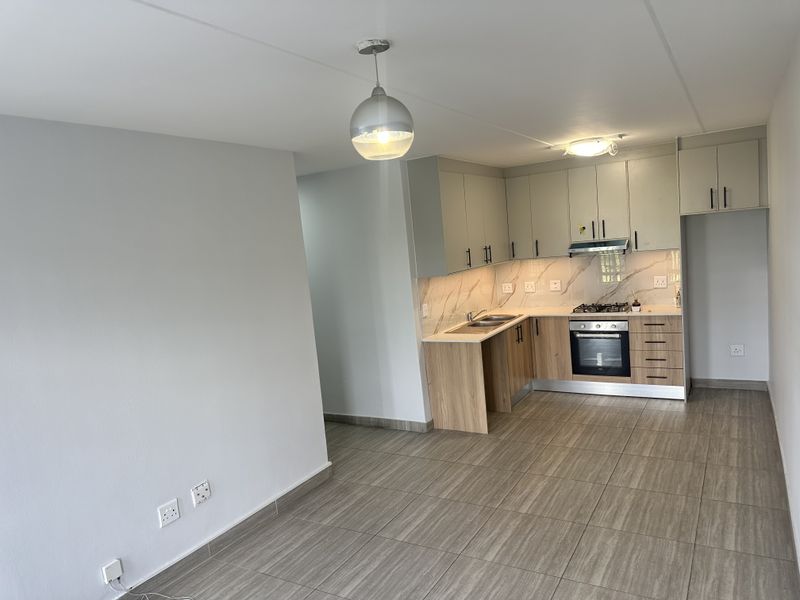 Modern open-plan kitchen featuring sleek cabinetry, stone-look backsplash, integrated gas hob, oven, and extractor fan, complemented by neutral tiled flooring throughout.