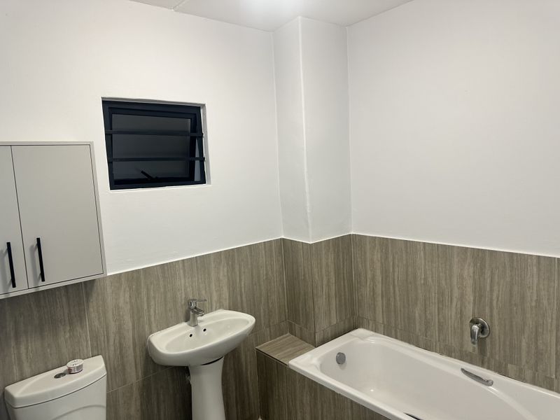 A clean, modern bathroom featuring a pedestal washbasin, a bathtub with tiled surround, and a wall-mounted storage cabinet.